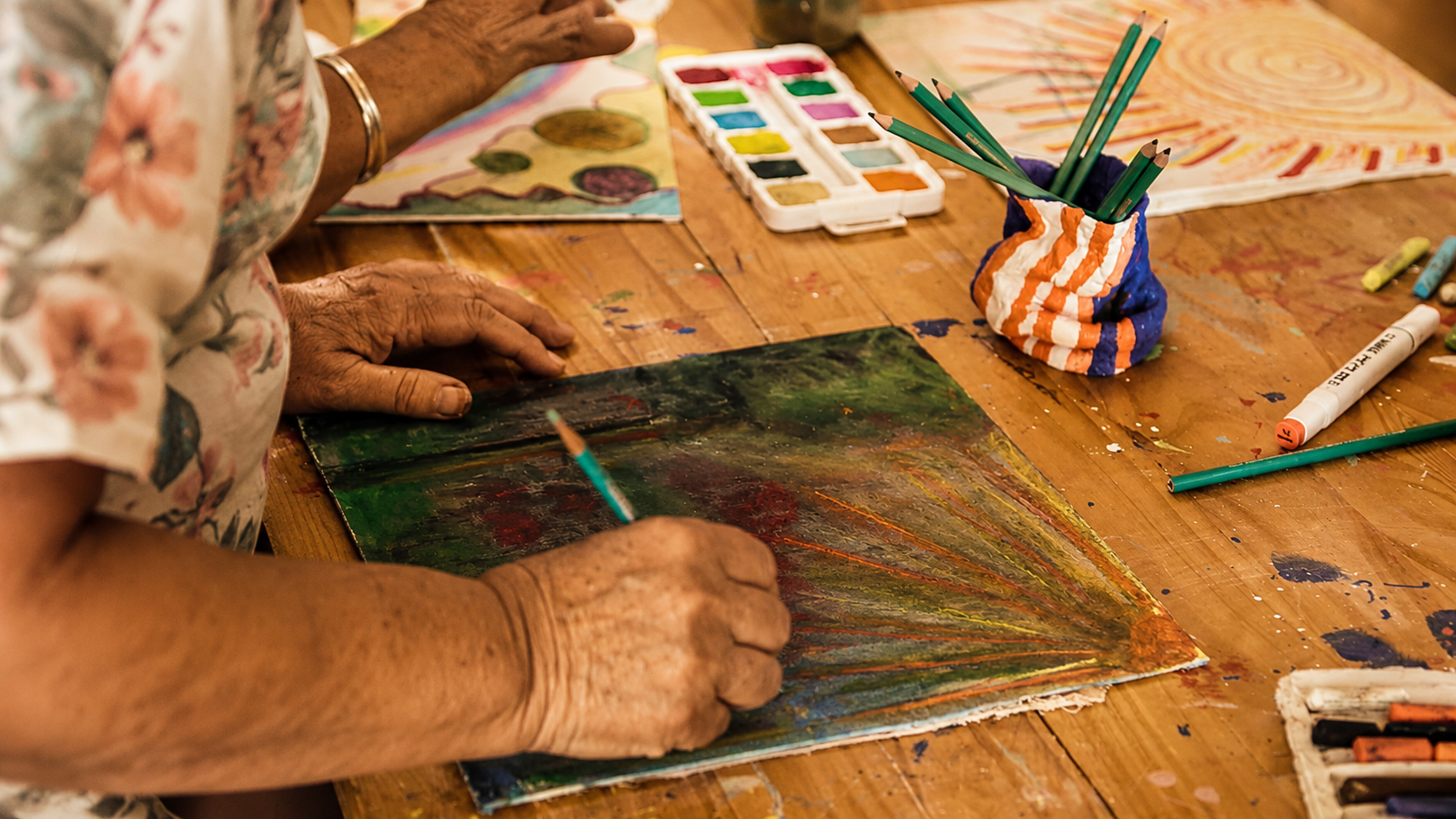 Hands working with colour and material at the atelier table.