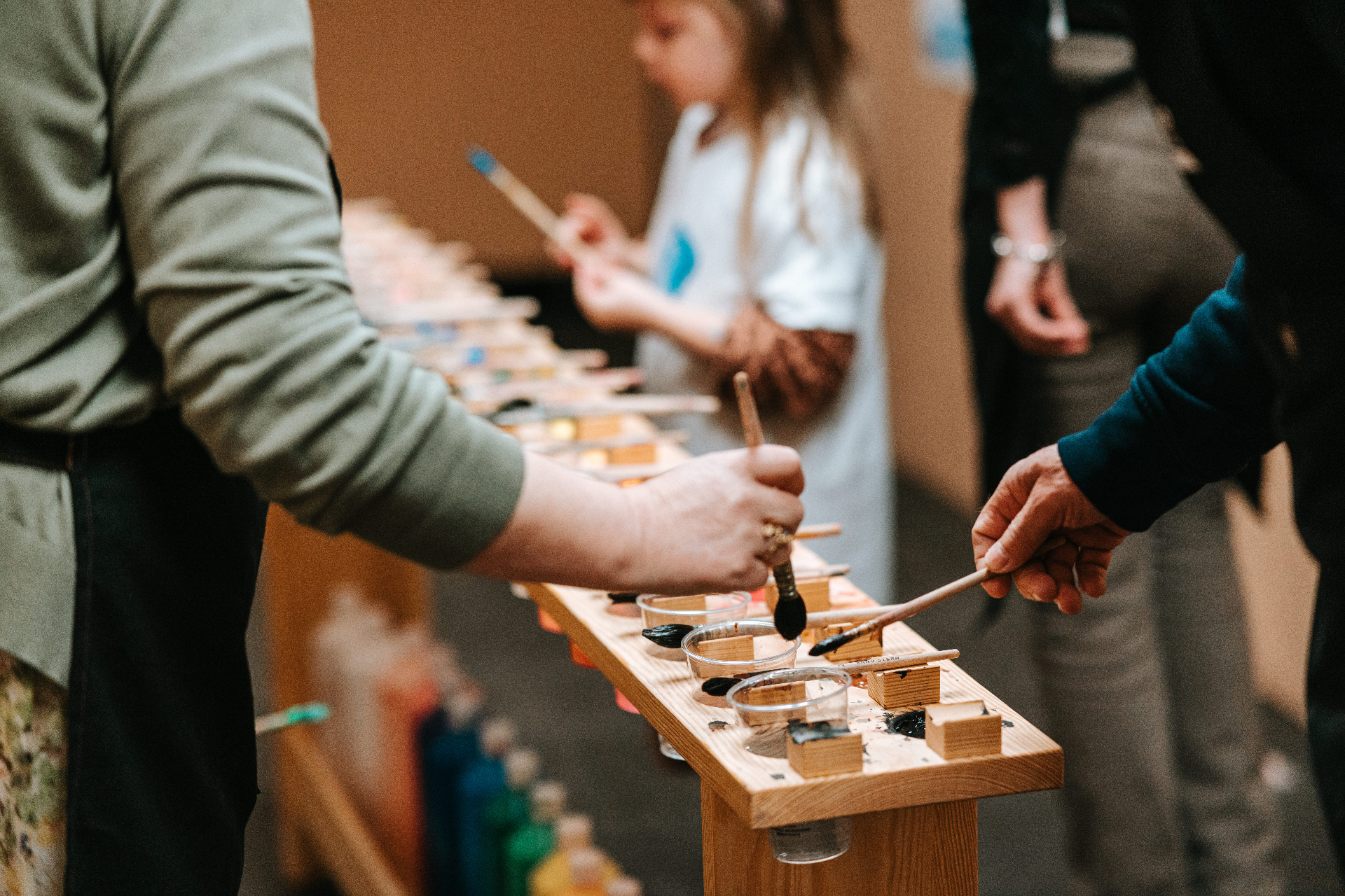 Hands painting at a long narrow wooden setup during a group atelier.